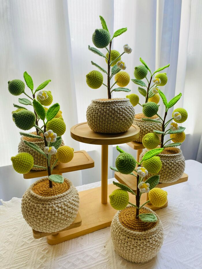 A display of several potted crochet lemon trees with green and yellow lemons and white flowers, showcasing incredible crochet art.