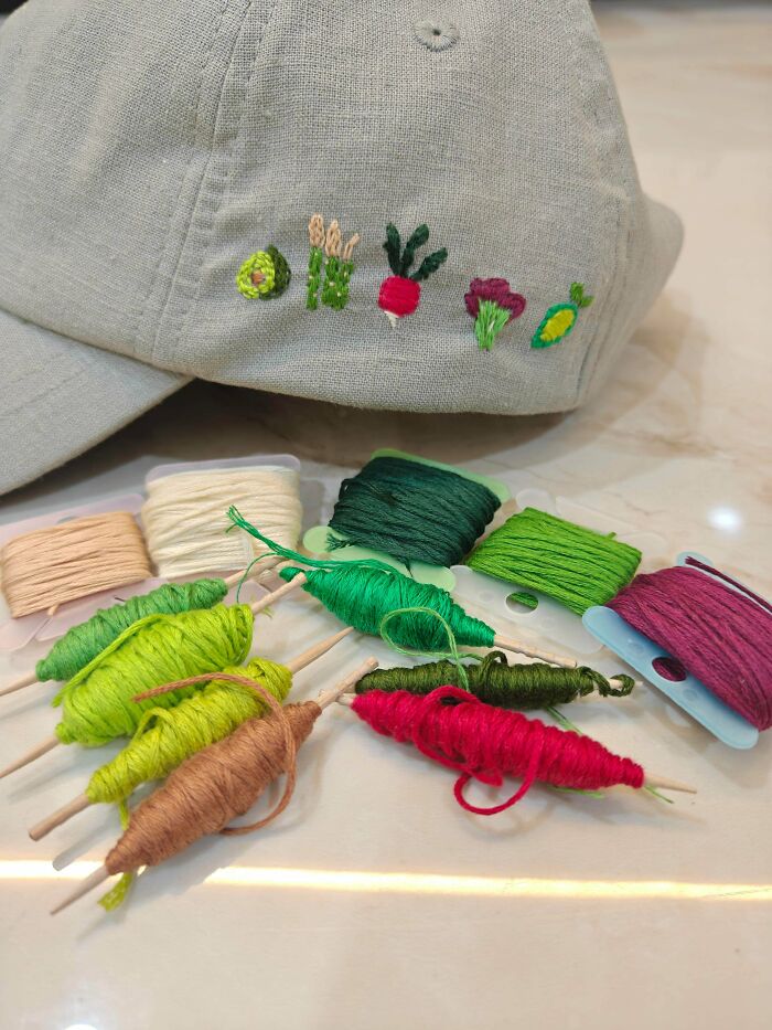 A grey cap with small embroidered vegetable designs shown next to colorful embroidery floss spools