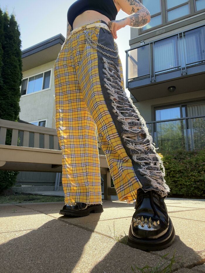 A person wearing wide-leg pants with yellow plaid and ripped black fabric, made out of things thrown away.