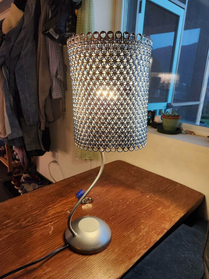 A modern desk lamp with a cylindrical shade made from upcycled metal can tabs, creating unexpected lighting.