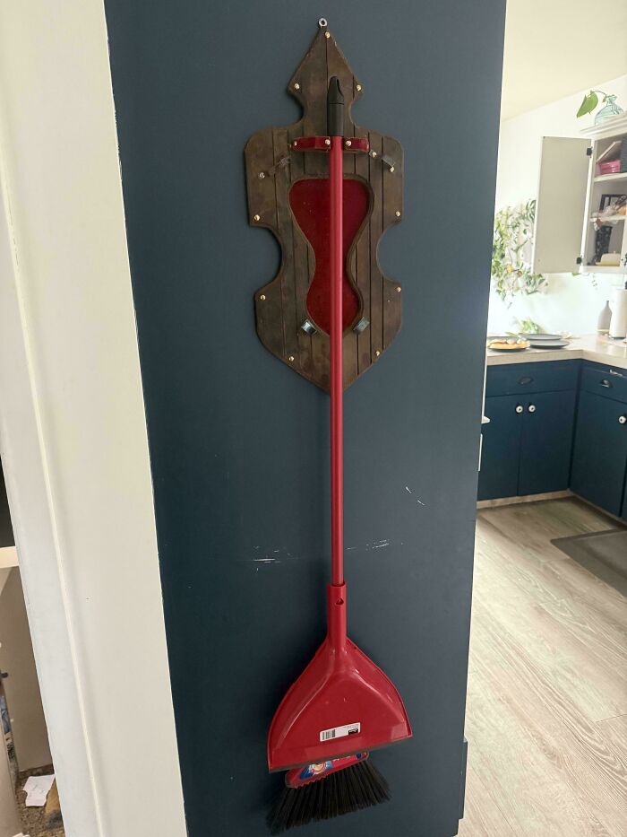 Red broom and dustpan hanging on a decorative wooden wall mount, an inventive way things made out of things that would have been thrown away can be displayed.