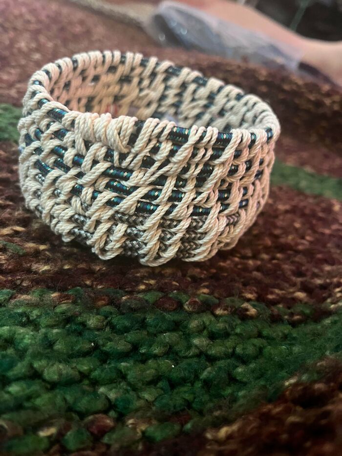A small, intricately woven basket, crafted from things that would've been thrown away, rests on a textured surface.