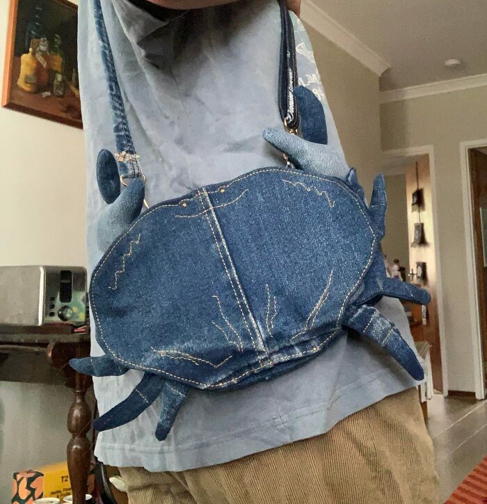 A person wearing a denim crab-shaped bag, made out of things that would’ve been thrown away, slung over their shoulder.
