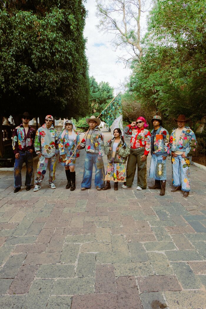 A group wearing colorful outfits made out of things that would’ve been thrown away, standing on a cobblestone path.