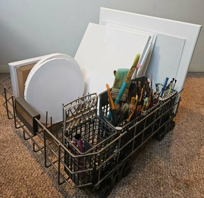 A metal dishwasher rack repurposed as a holder for art supplies, with paintbrushes and canvases, a creative use of thrown away items.
