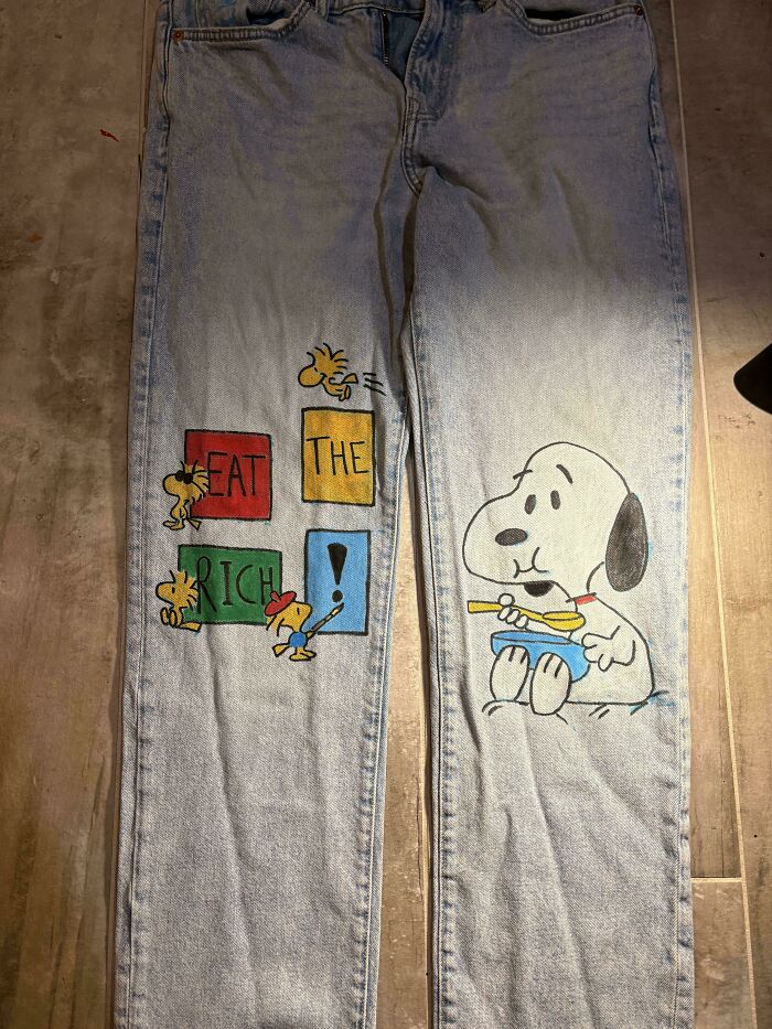 A pair of light blue jeans with a custom painting of Snoopy and friends, made from things thrown away.