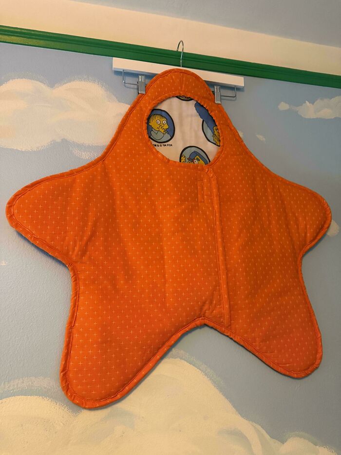 An orange star-shaped baby sleeping bag with a cartoon character inside, made out of things that would've been thrown away.