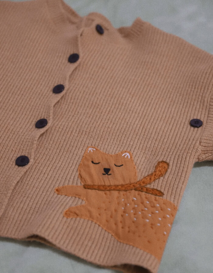 A close-up of a baby's cardigan with an embroidered cat design, made out of things that would've been thrown away.