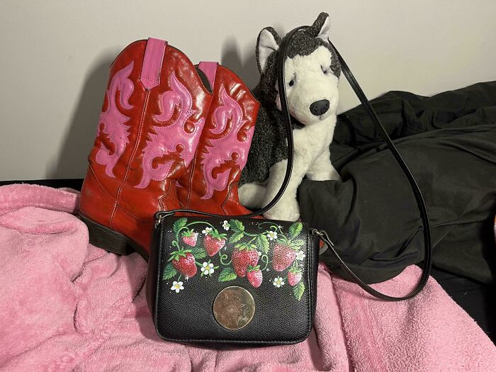 A black purse with a strawberry design, red and pink cowboy boots, and a husky plush toy, unexpected things made out of things that would've been thrown away.