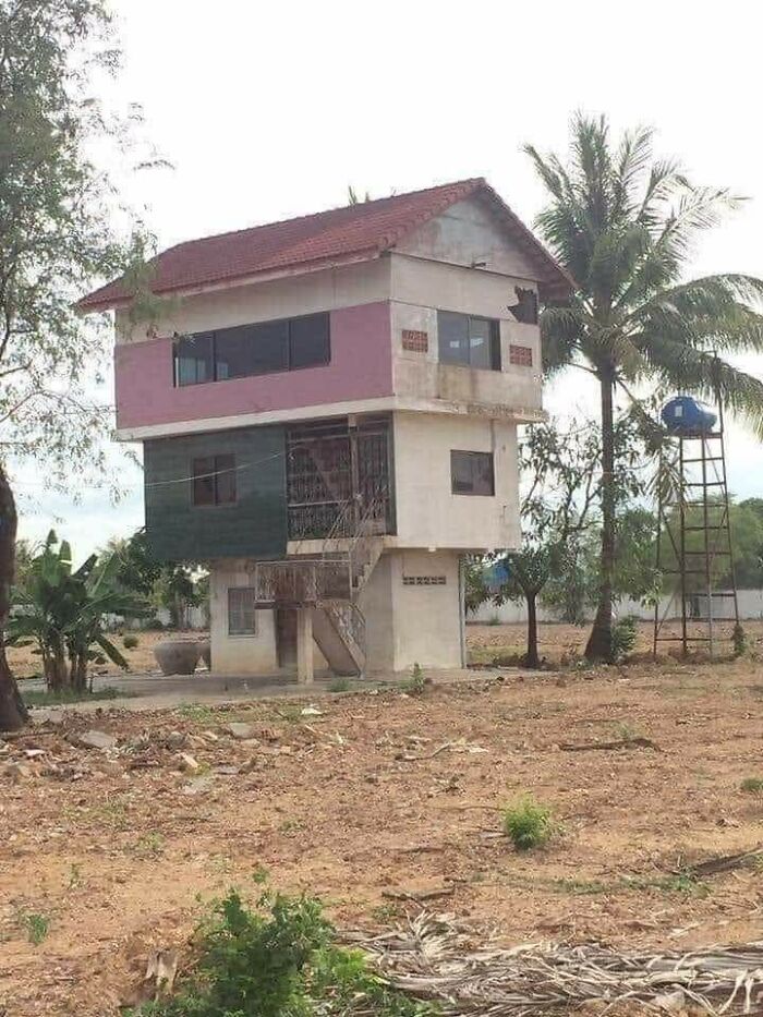 A multi-story house with mismatched sections and a small car on a tall ladder structure nearby, an architecture design fail.