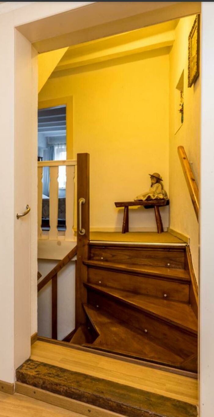 An awkward, winding wooden staircase with a low ceiling and a small decorative bench, highlighting an architecture design fail.