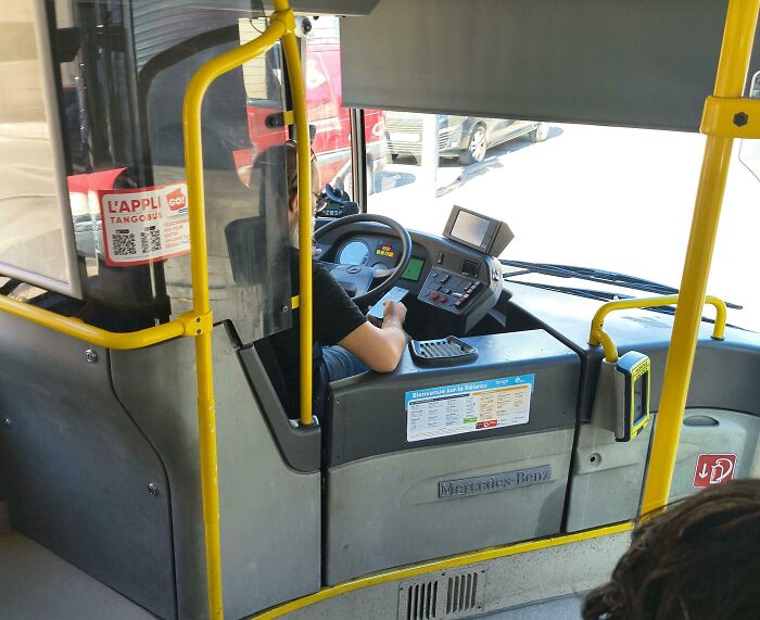 A bus driver looks at their phone, showcasing a lack of basic human decency by being distracted while driving.