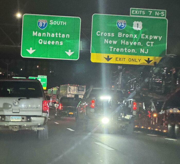 Nighttime traffic jam under highway signs for Manhattan, Queens, and Cross Bronx Expy, highlighting a lack of basic human decency.