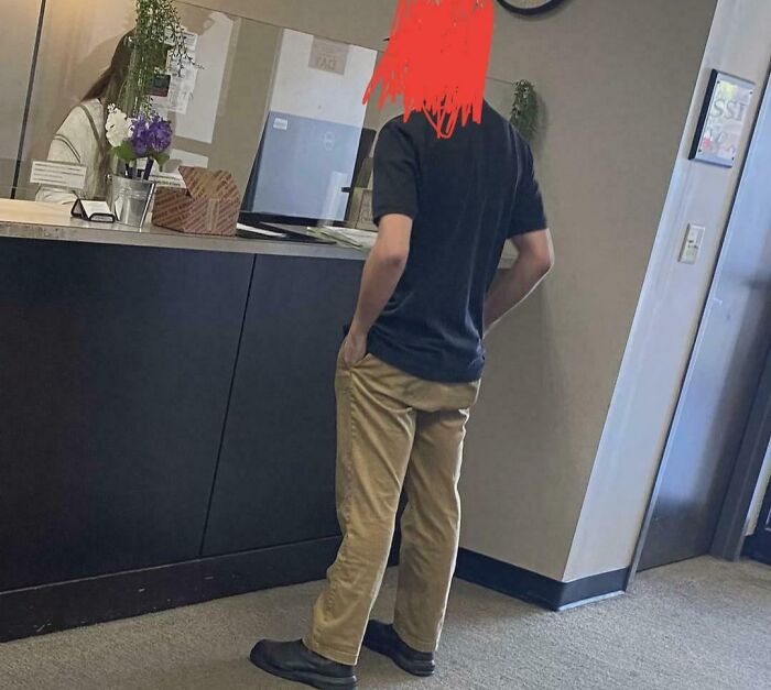 A person with red scribbled hair stands facing away from the camera in an office, demonstrating a lack of basic human decency.