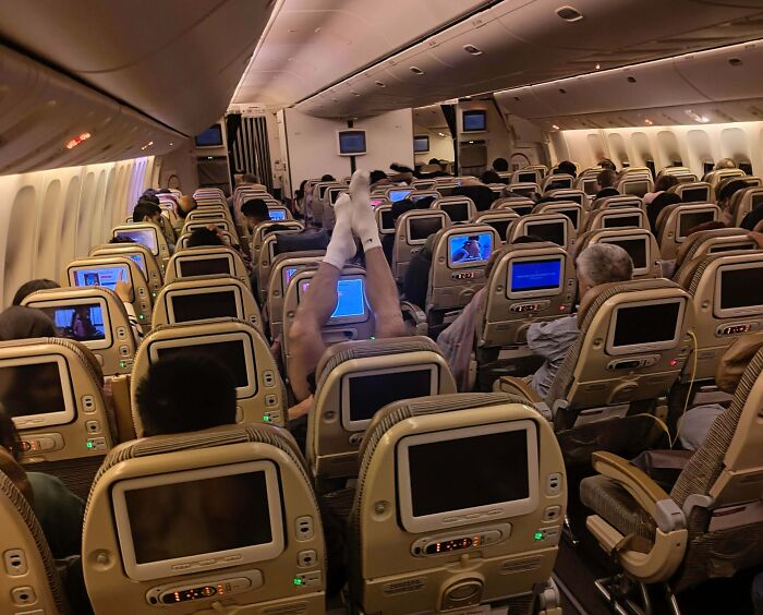 An airplane cabin showing a passenger with feet propped up on the seat in front, an example of lacking basic human decency.