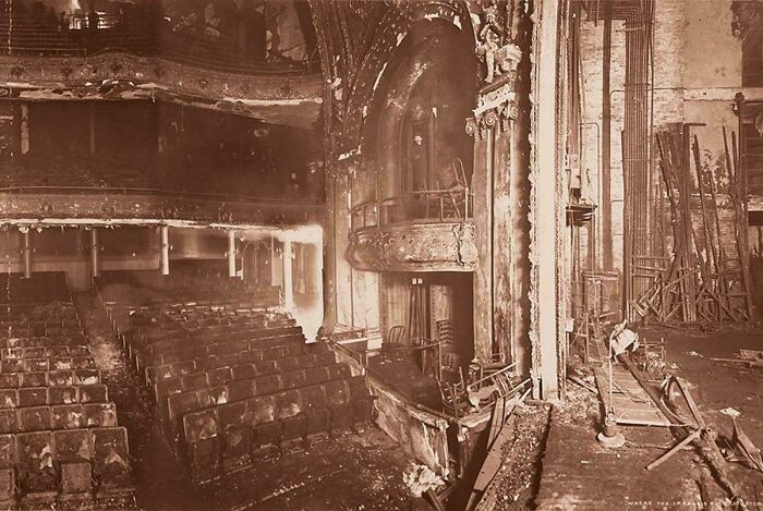 A historical photo of a severely damaged theater interior, showing charred seats and debris, feeling almost impossible to explain.