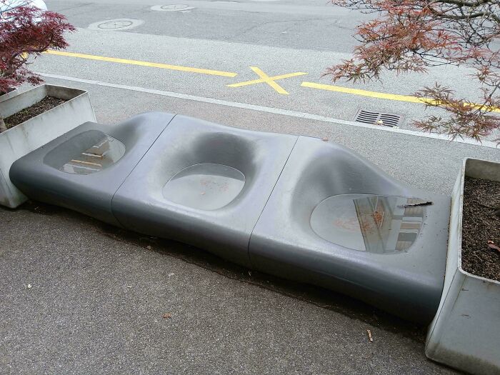 A modern outdoor bench with three concave sections filled with water, illustrating an architecture design fail.