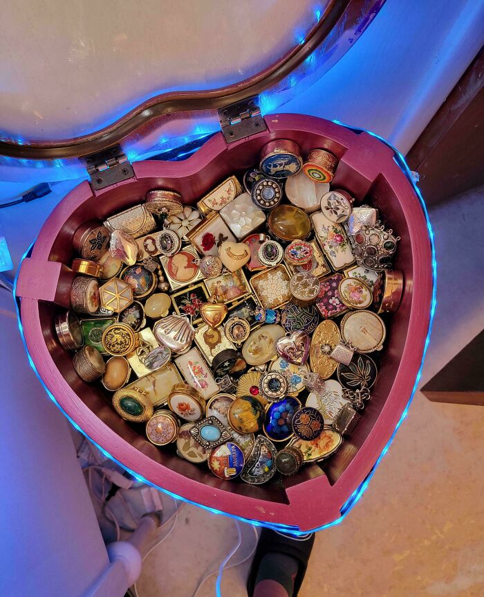 A heart-shaped box overflowing with a fascinating collection of vintage rings, brooches, and small decorative items, illuminated by blue lights.