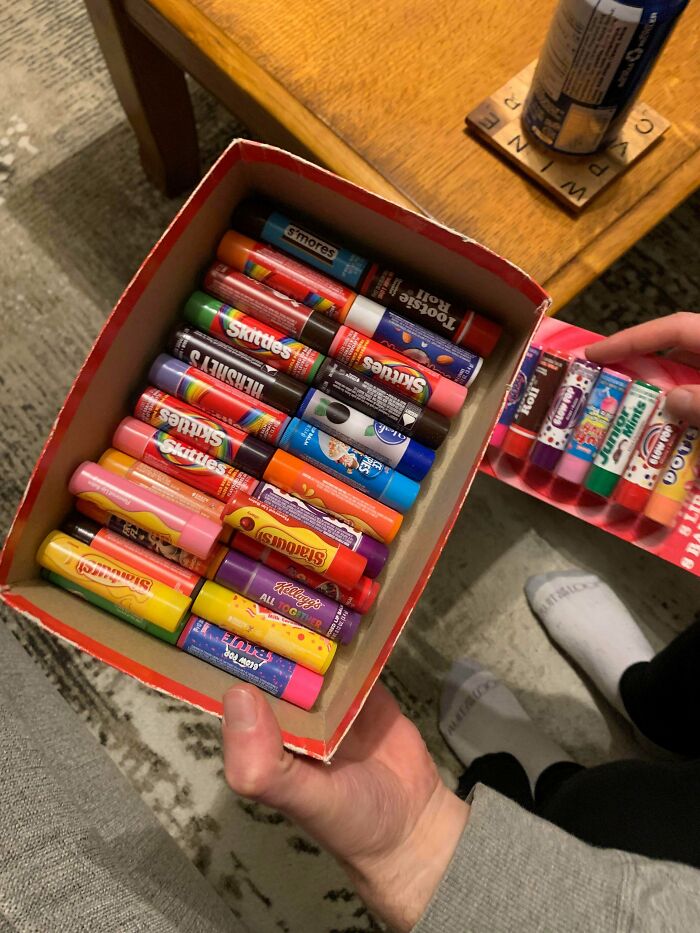 A person holding a box filled with a fascinating collection of various flavored lip balms.