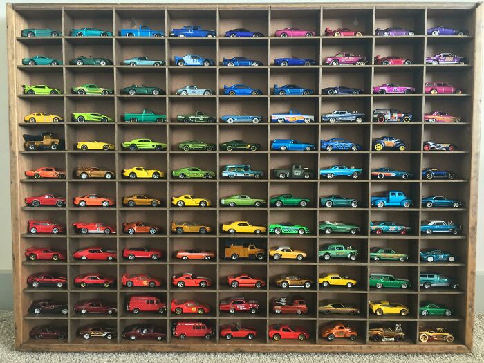 A vast collection of colorful toy cars neatly displayed in a wooden shelf, showcasing fascinating collections.