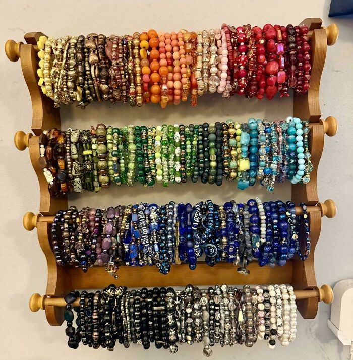 An organized collection of colorful beaded bracelets displayed on a wooden wall rack, sorted by color.