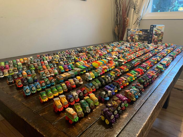A huge collection of Thomas the Tank Engine toy trains spread across a wooden table, showcasing unexpected collections.