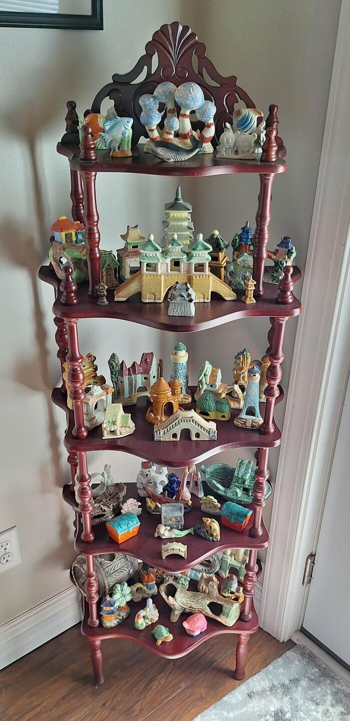A fascinating collection of miniature ceramic village buildings and figures displayed on a multi-tiered wooden shelf.