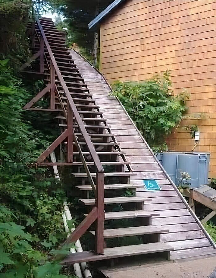An extremely long, steep wooden ramp with stairs and a wheelchair access sign, illustrating an architecture and design fail.