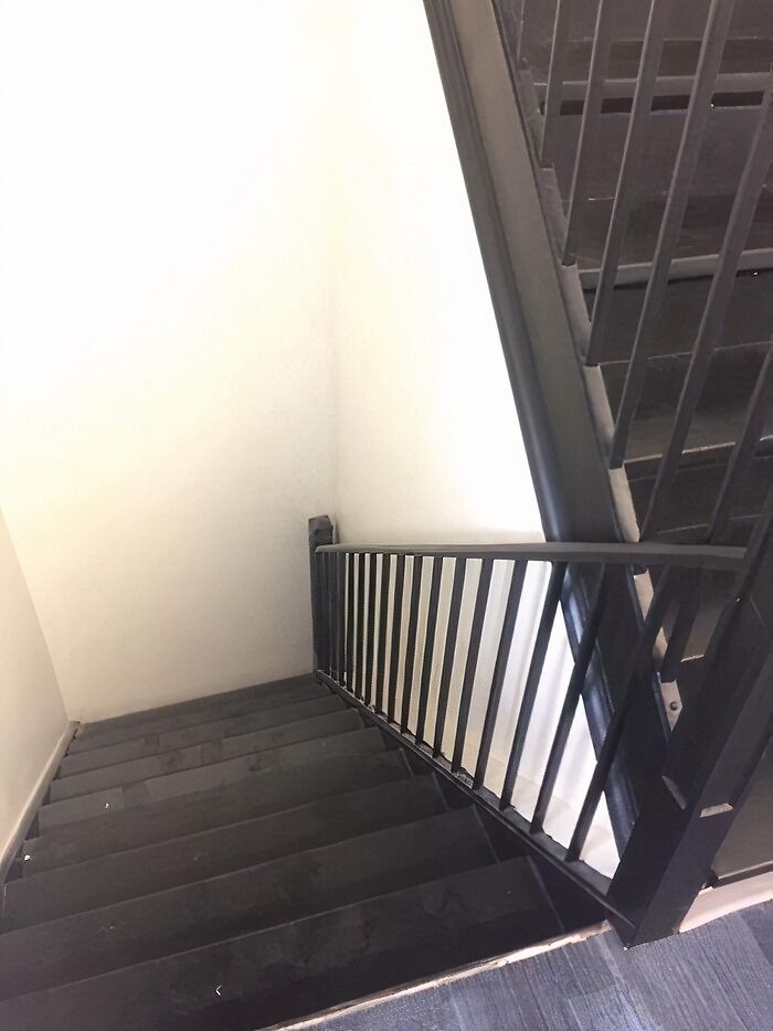 A dark staircase with a railing that abruptly stops before the bottom step, an architecture and design fail.