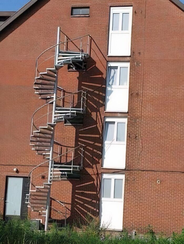 A red brick building features a metal spiral fire escape that doesnt align with the windows, an architecture fail.