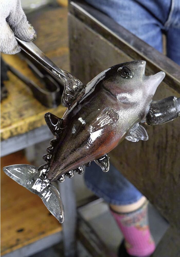 Japanese artist creates hyper-realistic glass food, a dark, detailed glass fish sculpture held by a tool.