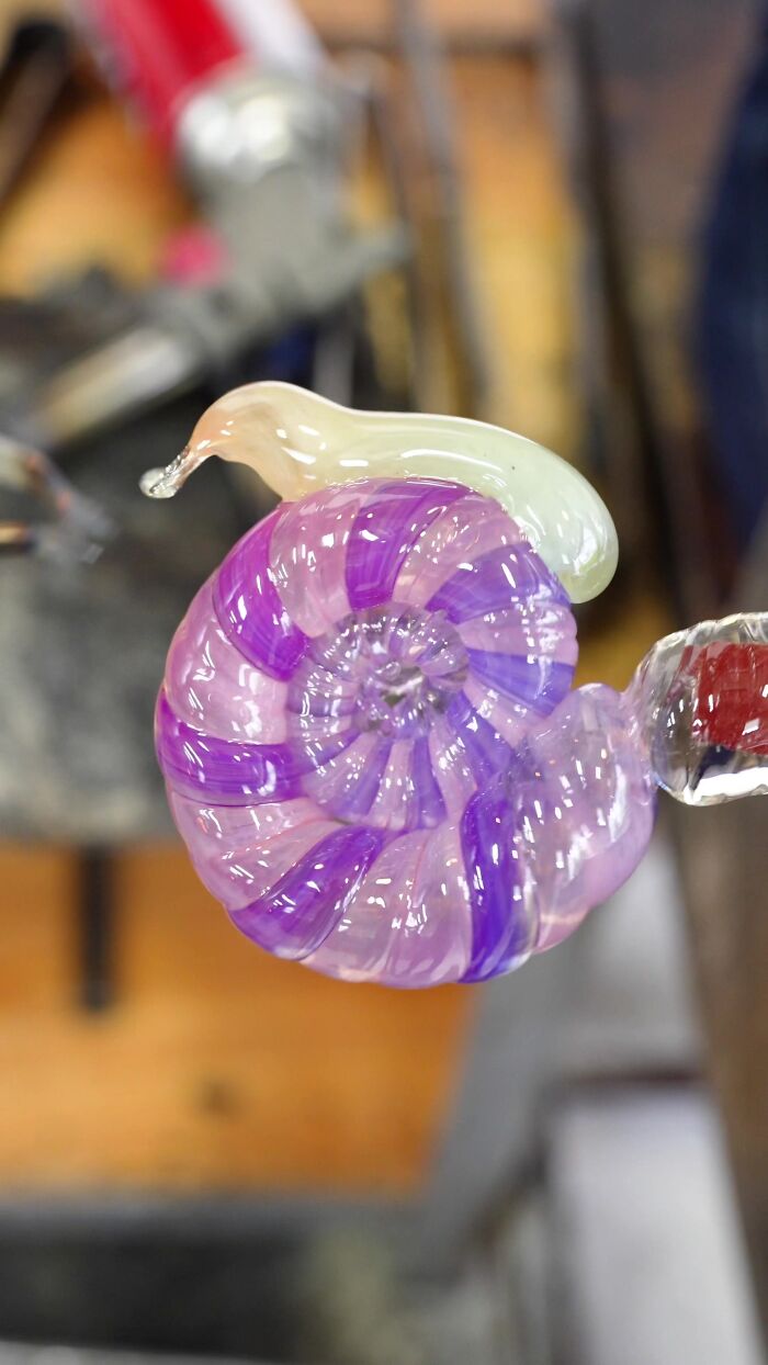Japanese artist creates hyper-realistic glass food, a vibrant purple and pink glass snail sculpture held by tools.