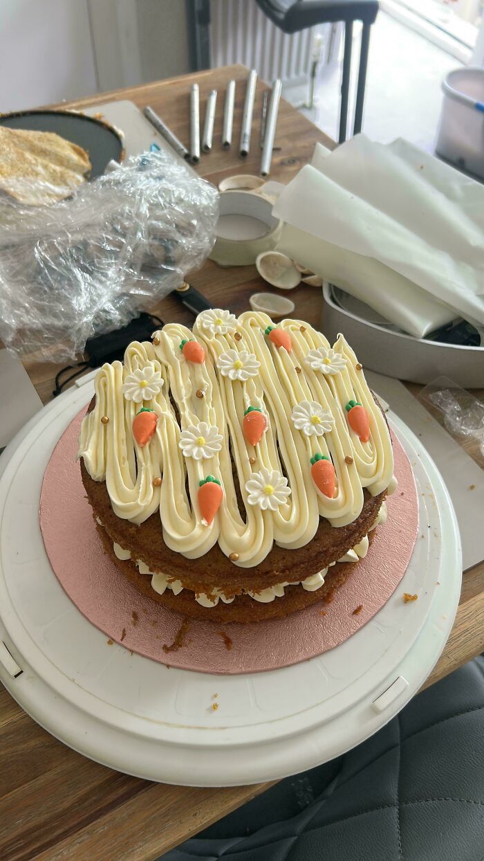 A beautifully decorated carrot cake treat with cream cheese frosting, mini carrots, and daisies.