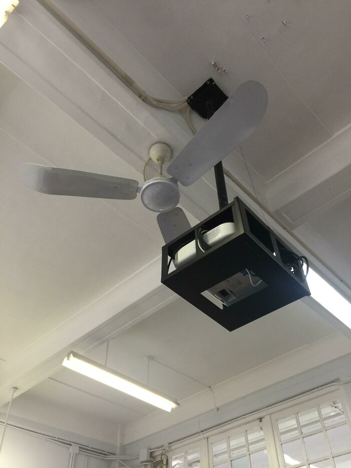 A projector mounted directly in front of a ceiling fan, proving common sense isn't common.