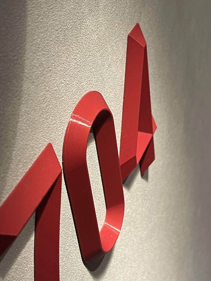 A close-up of functional 3D prints forming red numbers 104 on a gray wall, making everyday life much easier with clear labeling.
