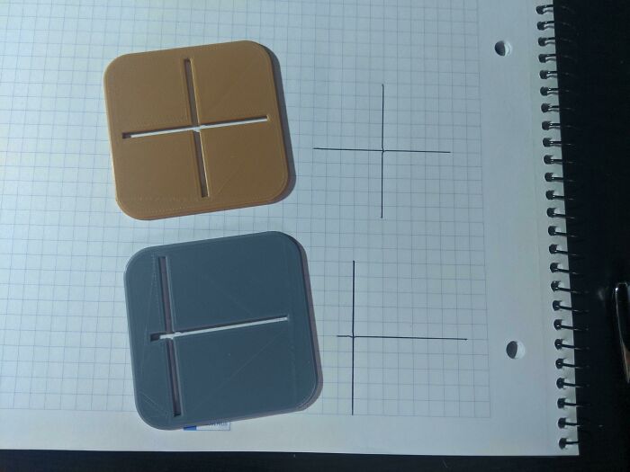 Two square functional 3D prints, one brown and one gray, resting on graph paper with drawn crosshairs, making everyday life much easier for precision.
