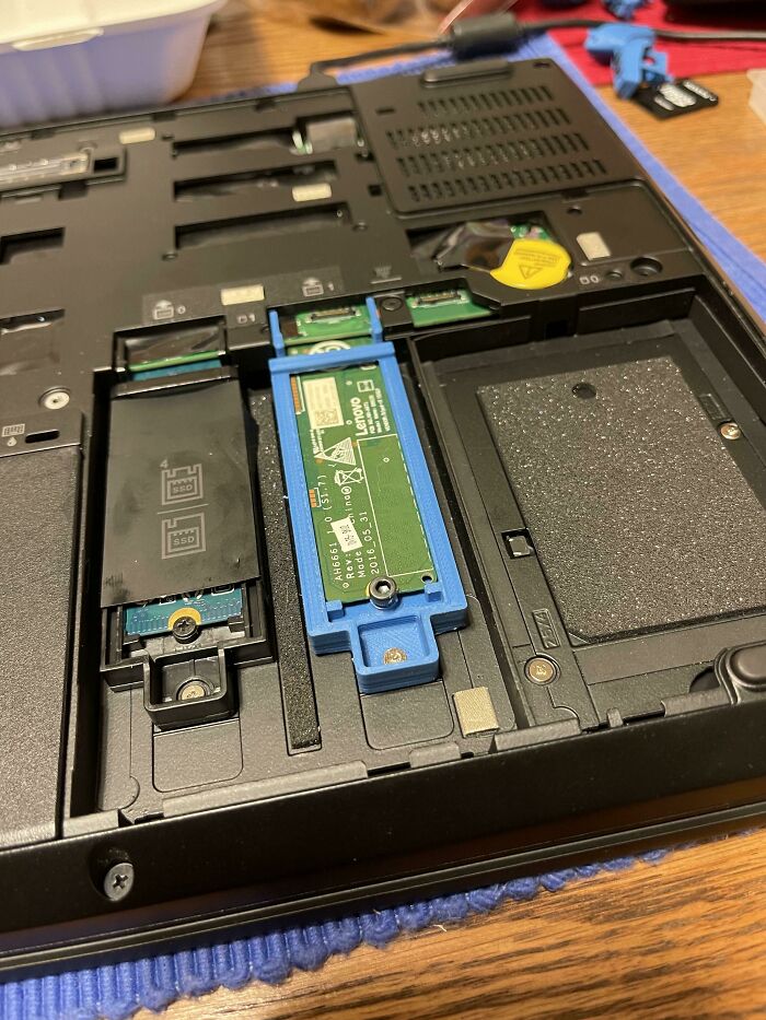 A close-up of a laptop's interior showing a blue 3D print SSD caddy, making everyday life tech repairs easier.