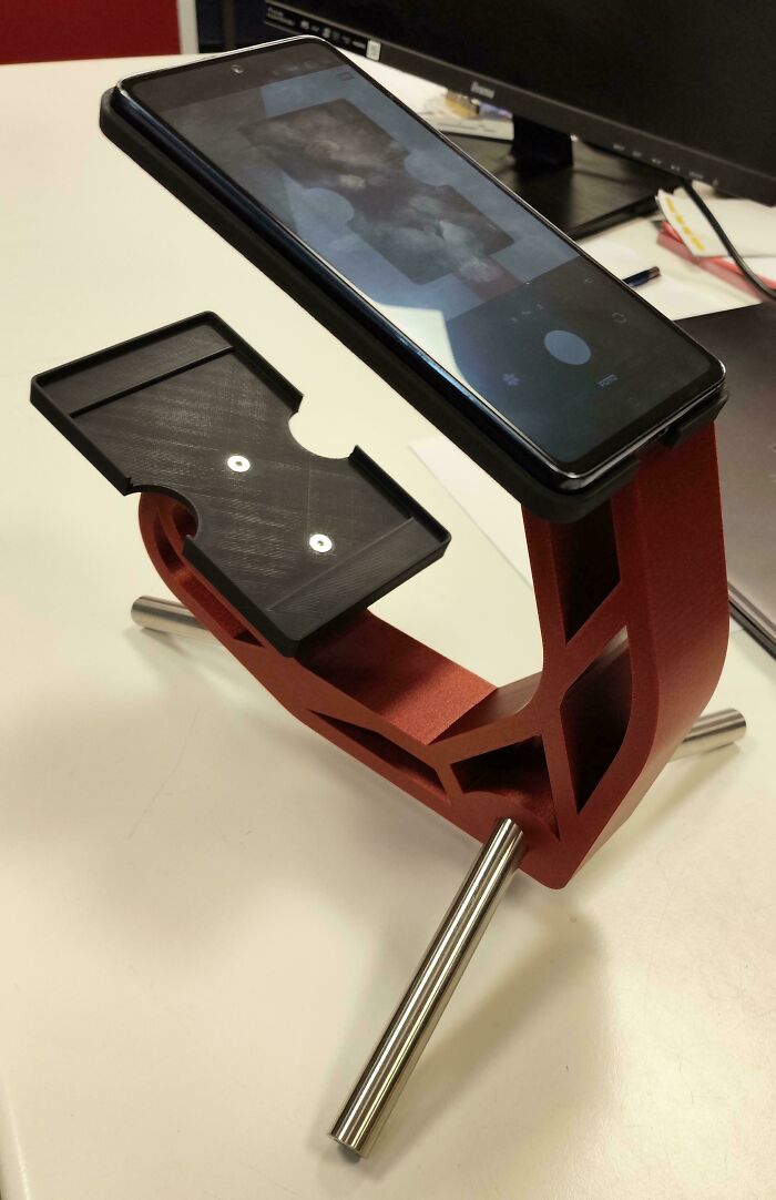A red and black stand holding a smartphone, demonstrating functional 3D prints to make everyday life easier.