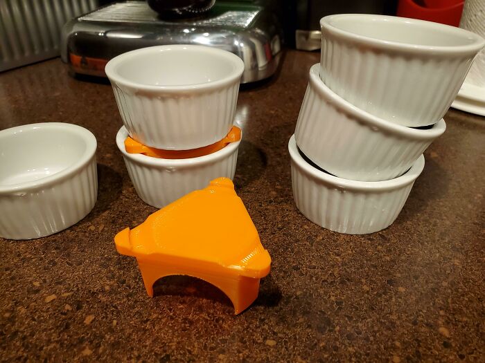 An orange 3D print acting as a stand for ramekins, a practical solution for easier everyday use.
