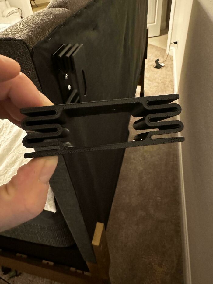 A hand holding a black 3D printed bracket, designed for functional use on furniture, making everyday life easier.