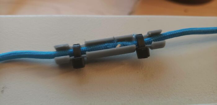 A close-up of a blue cable secured with several small, gray 3D printed clips, a functional print for organization.