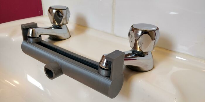 A grey 3D printed faucet extender connecting two sink faucets, making everyday life much easier.