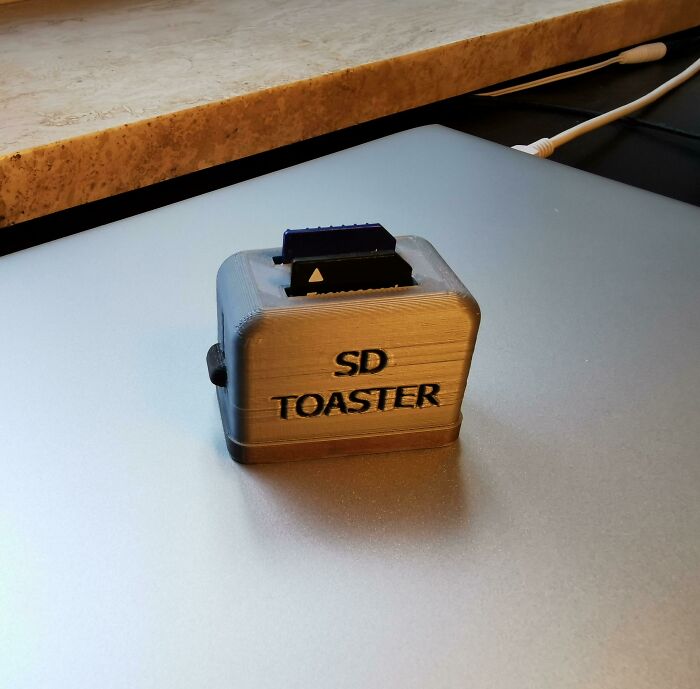 A grey 3D printed SD toaster, a functional 3D print acting as an SD card holder, sitting on a silver laptop.