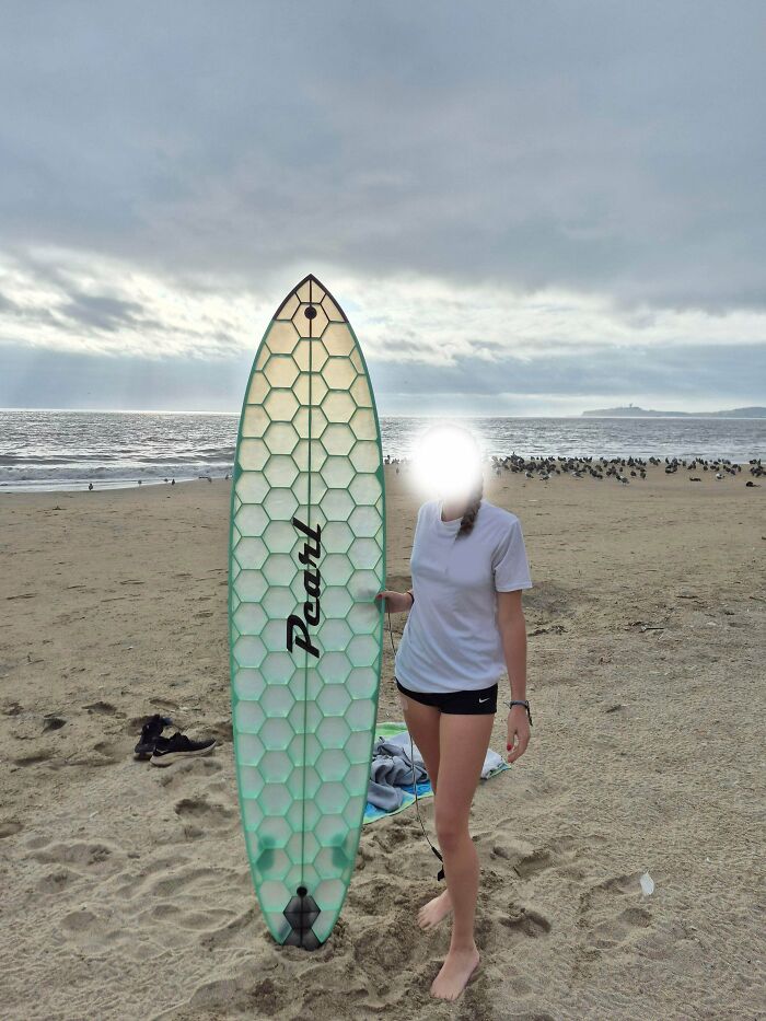 A person standing on a beach with a surf-board featuring a honeycomb pattern, showcasing functional 3D prints.
