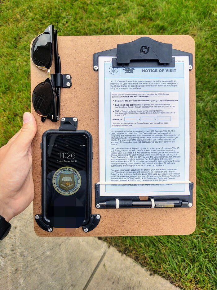 A hand holding a functional 3D print clipboard with a smartphone and sunglasses attached for everyday life.