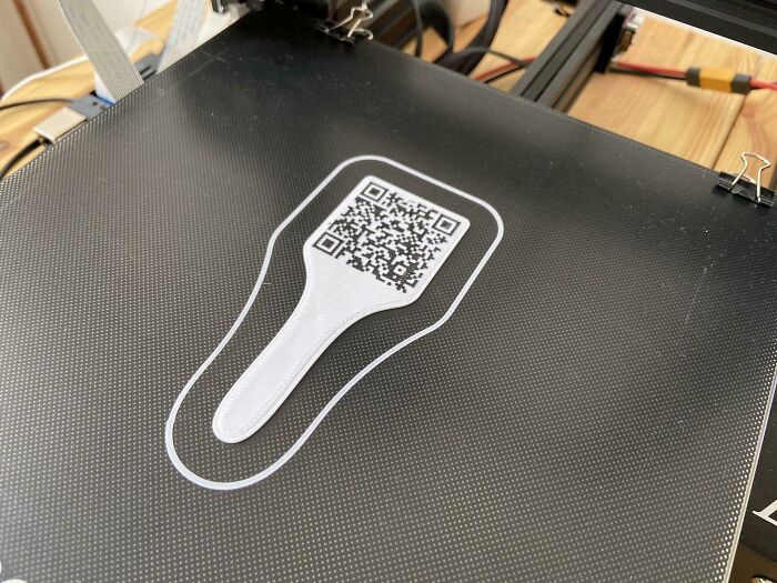 A white, functional 3D print with a QR code on a 3D printer bed, making everyday life easier.