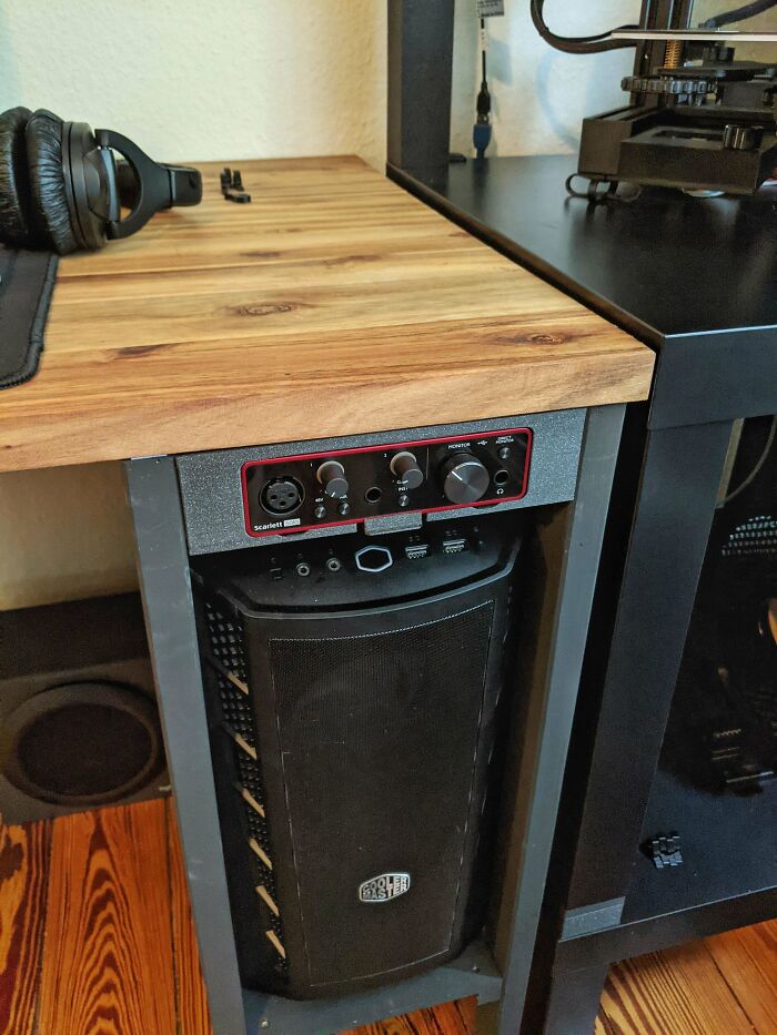 A functional 3D print: a custom-fitted audio interface and PC case holder under a wooden desk.