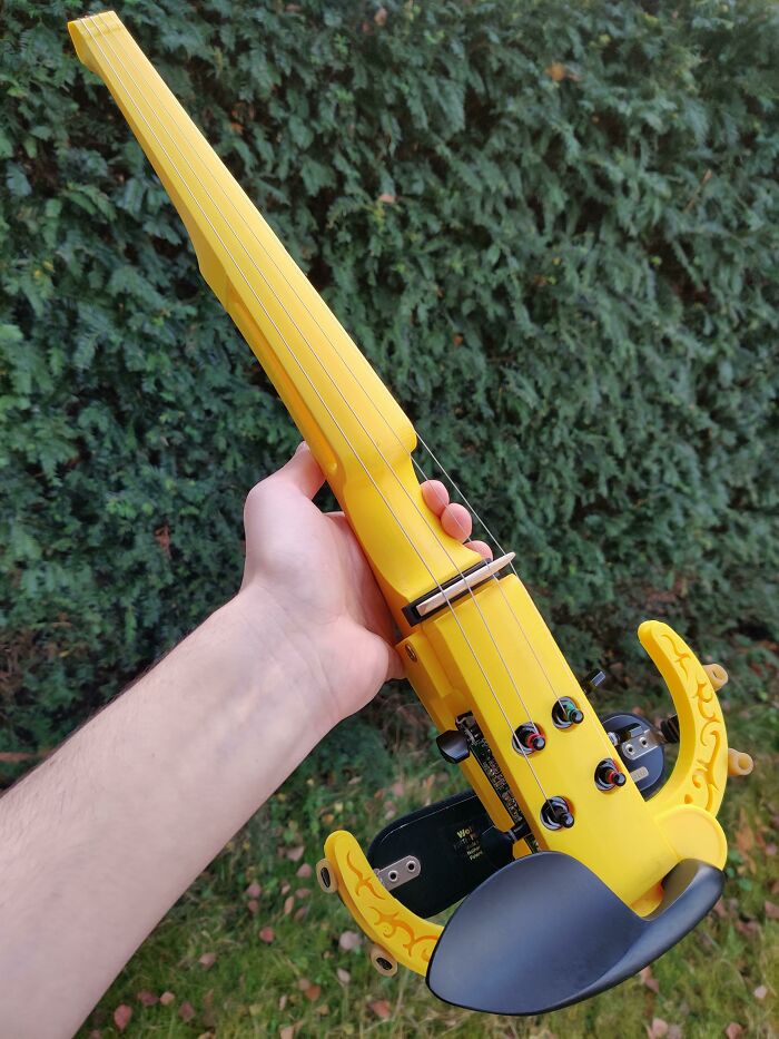 A hand holding a bright yellow 3D print of an electric violin, a functional 3D print for music.