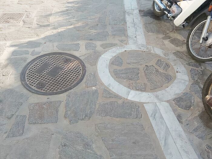 A manhole cover not aligned with a circular stone design on a pavement, showcasing a You Had One Job fail.