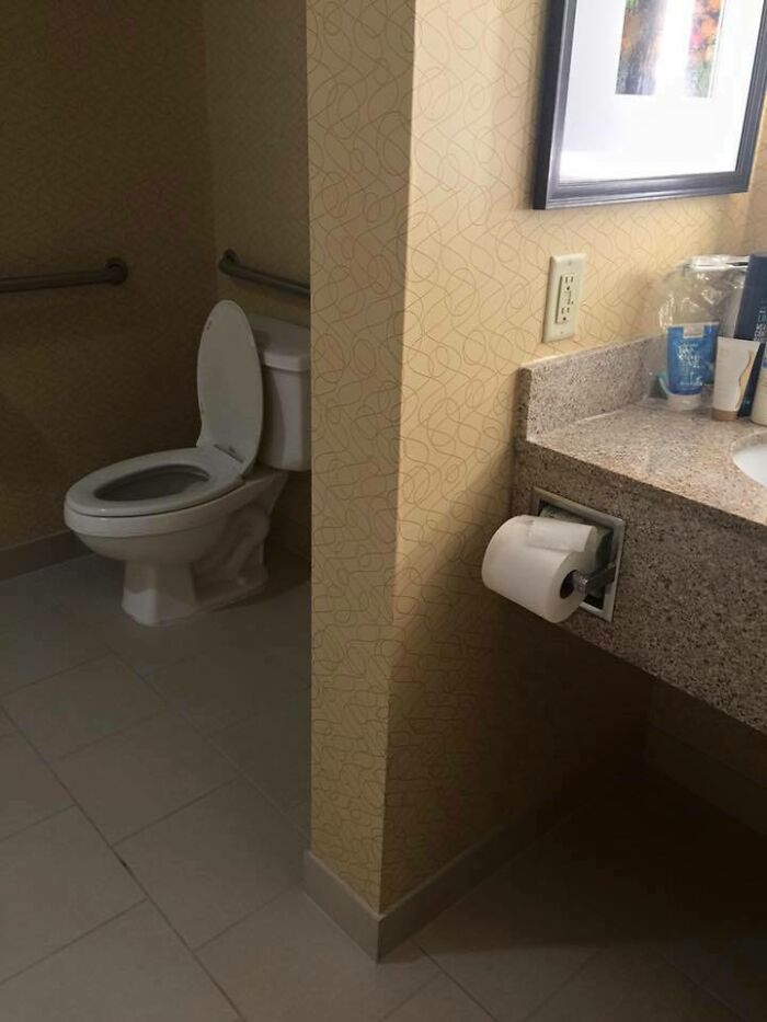 A toilet in a bathroom with the toilet paper dispenser inconveniently located behind a wall, a common sense fail.